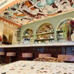Sacha est le restaurant bistronomique et bar à cocktails de l'hôtel Posidonia à Nice. Il propose une cuisine méditerranéenne créative dans un décor habillé des fresques de l'artiste Franck Lebraly (comptoir)